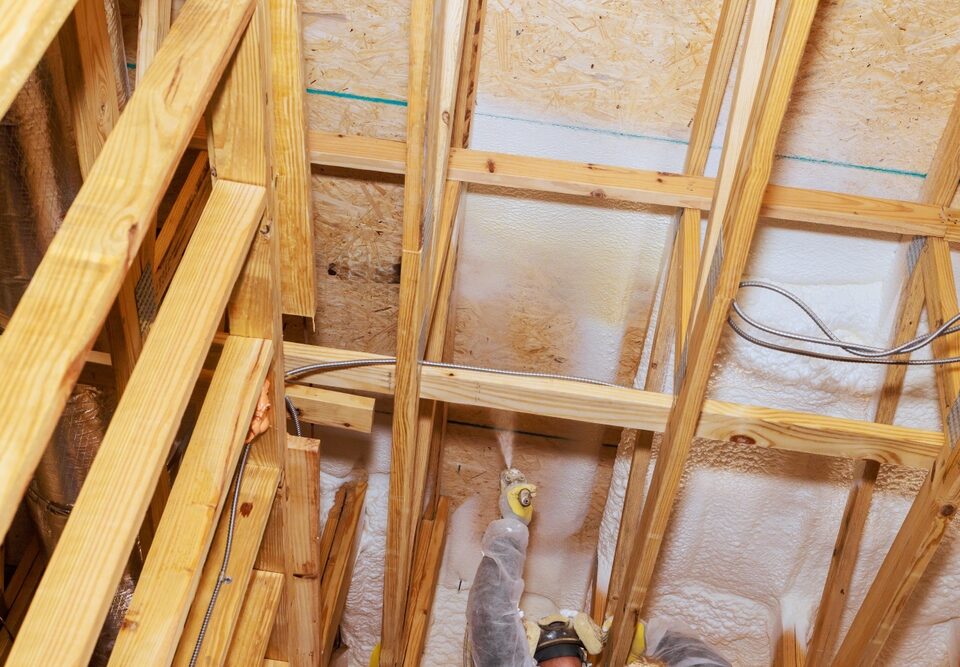 A worker installing spray foam insulation on a ceiling